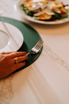 Person reaching for a silver fork on a green placemat during a dinner service in a restaurant