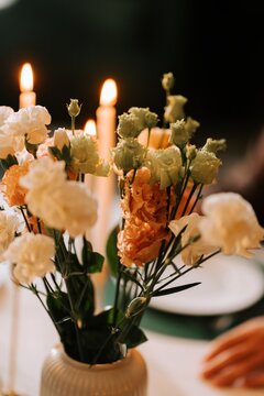 Bouquet of flowers in a vase placed on a dinner table with glowing candles during an evening meal