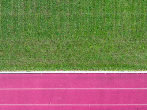 Aerial view of a pink running track adjacent to a vibrant green grass field in Latvia.