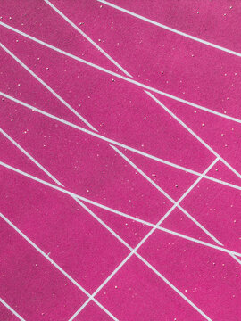 Aerial view of a vibrant pink sports track with intersecting white lane markings and textured surface in Latvia.