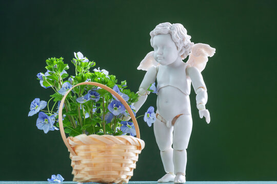 White miniature cupid doll with basket of blue spring Veronica flowers, selective focus
