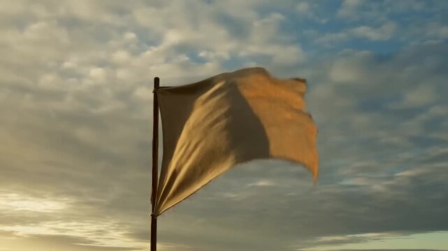 Plain burlap flag billows from a pole beneath a warm, cloudfilled evening sky