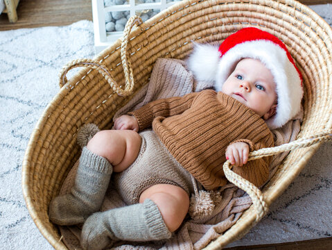 Cute baby dressed as Santa Claus at home during Christmas, enjoying a cozy festive atmosphere near a decorated Christmas tree.