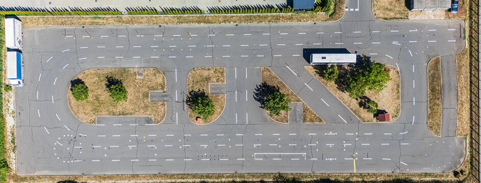 Aerial view of a driving test track with asphalt lanes, practice routes, parked trucks, and landscaped traffic islands in Eger, Hungary, during summer.