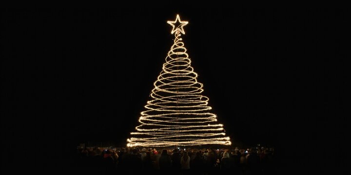Long exposure light painting of a christmas tree shape with a glowing star topper against a black background
