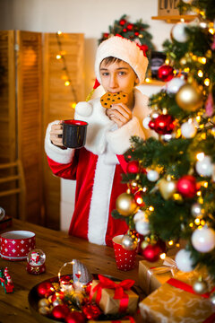 Teenage boy dressed as Santa&rsquo;s helper posing near a decorated Christmas tree at home, creating a cheerful and festive holiday atmosphere.