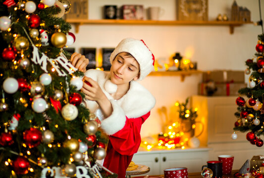 Teenage boy dressed as Santa&rsquo;s helper posing near a decorated Christmas tree at home, creating a cheerful and festive holiday atmosphere.