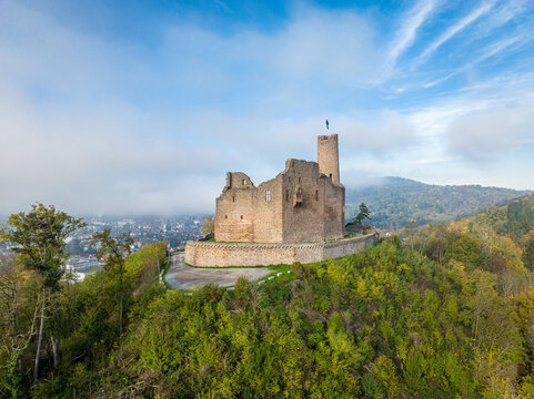 Aerial view of Windeck Castle ruins perched on a hill surrounded by autumn forest with patches of fog and a clear blue sky in Weinheim, Baden-Wurttemberg, Germany.