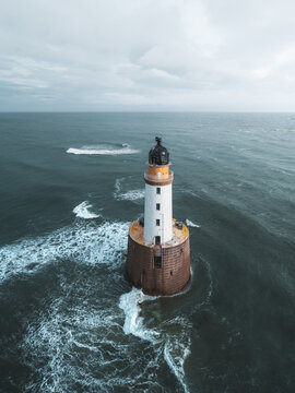 Aerial view of Rattray Head Lighthouse surrounded by the North Sea with waves crashing against its base in Peterhead, United Kingdom.