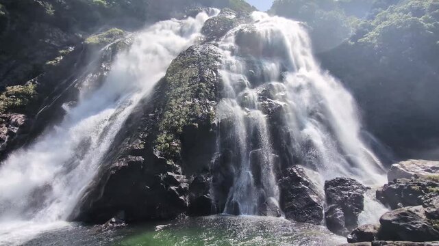 the Okonotaki falls in the sunshine, surrounded by fresh, green vegetation 
