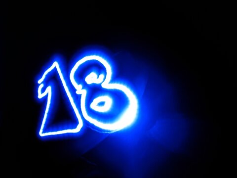 A blue neon light number eighteen drawn in light painting technique stands out against a pitch black backdrop. This abstract glowing electric digit is ideal for countdown and creative banner.