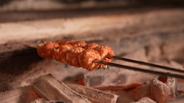 A chef is placing seasoned meat and chicken kebab skewers onto the hot charcoal grill station