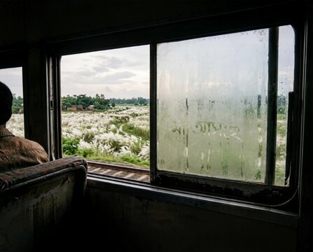 View from train window with Maa Asche text on glass and kash phool field in background