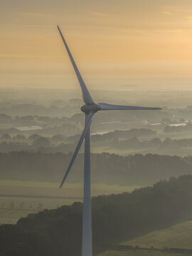 Aerial view of a wind turbine standing in a misty rural landscape during the golden hour in The Netherlands.