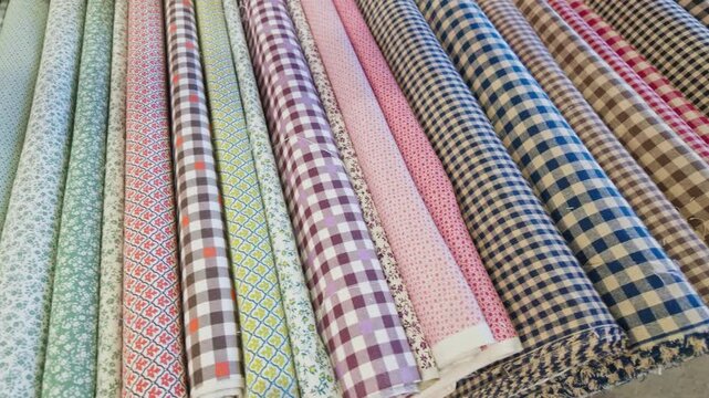 Assorted Rolls of Patterned Fabric With Floral and Gingham Designs Arranged in Rows