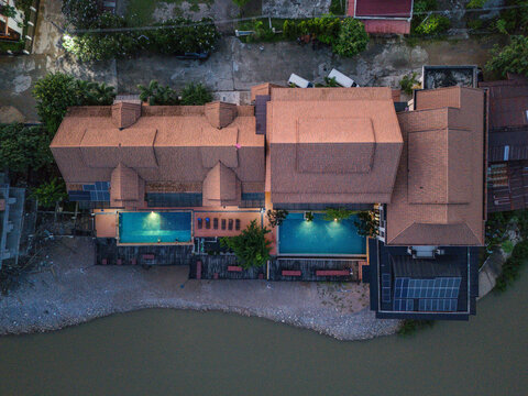 Aerial view of Don Khong resort with two illuminated swimming pools, wooden decking, and solar panels situated along the riverbank in Khong, Champasak Province, Laos.