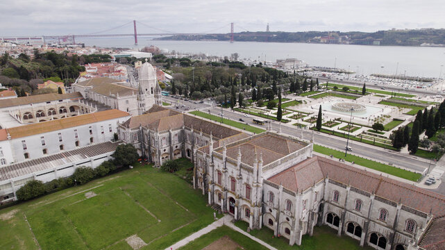 Aerial view of Jeronimos Monastery featuring ornate Manueline architecture, gardens, and the Tagus River with the 25 de Abril Bridge in the background in Lisboa, Lisboa, Portugal.