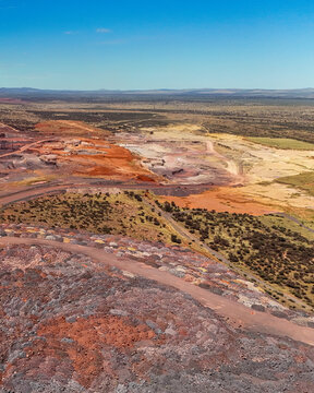 Aerial view of open-pit mining operations with massive piles of mine tailings, exposed mineral layers, and access roads cutting through the landscape in Rustenburg, North West, South Africa.