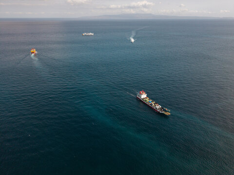 Aerial view of Pelabuhan Padang Bai with several ferries and cargo ships navigating the deep blue waters of the Bali Strait, Kecamatan Manggis, Bali, Indonesia.