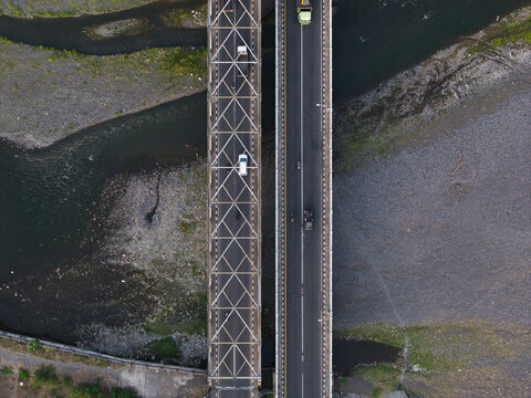 Aerial view of Jembatan Merah Proyek Pusat Kebudayaan Bali with two parallel bridges crossing a river, vehicles driving on the road, and rocky riverbanks in Klungkung, Bali, Indonesia.