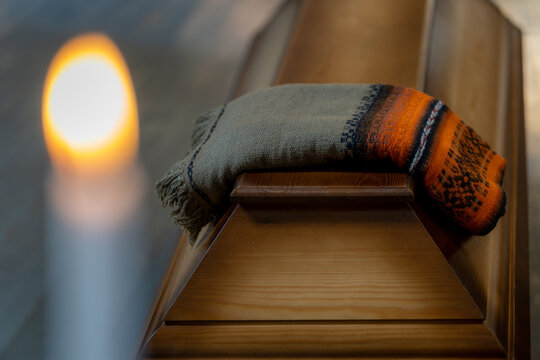 Folded Funeral Blanket on Wooden Coffin with Blurred Candle Flame