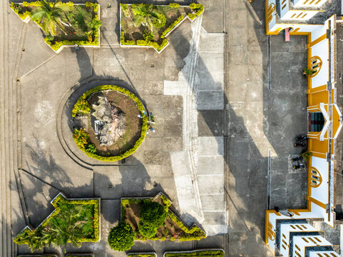 Aerial view of the central square in San Agustin featuring a circular garden, manicured hedges, and the yellow and white facade of the local church in San Agustin, Huila, Colombia.