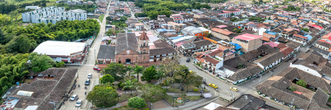 Aerial view of the historic town square and church surrounded by colonial buildings with terracotta roofs, lush green trees, and streets in San Agustin, Huila, Colombia.
