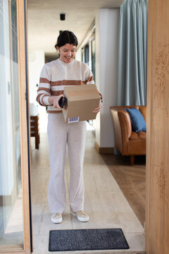 Woman holding cardboard box and scanning barcode with smartphone in doorway wearing striped sweater