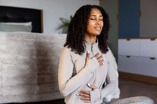 African American woman sitting on bedroom floor meditating in gray zip top near bed