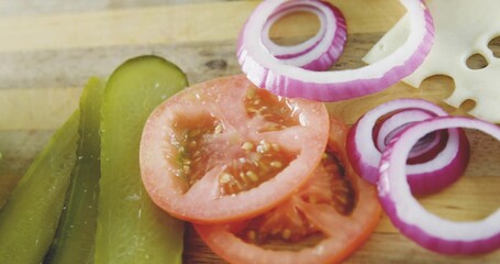 Displaying stack of sliced red tomatoes on wooden board, with pickles, onion rings, Swiss cheese © vectorfusionart