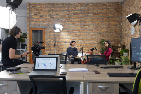 Diverse podcast hosts discussing research charts at studio table with microphones and laptop