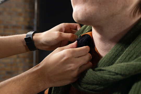 Diverse men adjusting black pom on green scarf and rust sweater, showing black smartwatch in studio