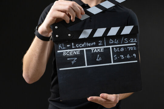 Male film crew member holding slate while wearing black polo and checking written notes in studio