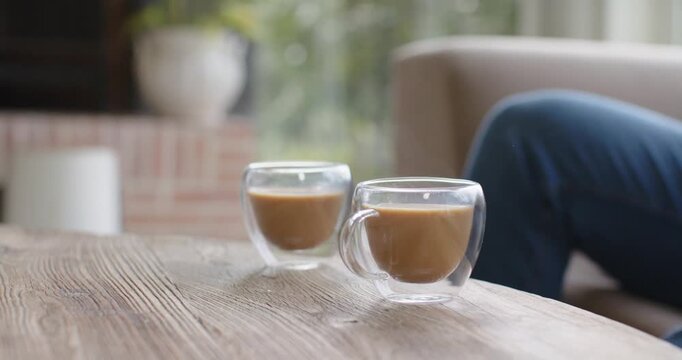 Camera is pushing forward, bringing two glass cups closer on wooden table to emphasize calm room