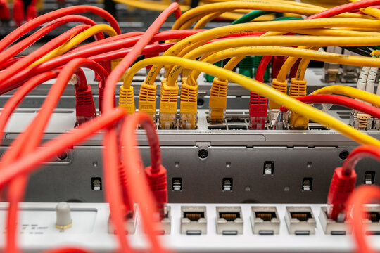 Disorganised tangle of Ethernet patch cables routed across network switches and patch panels inside a server rack, commonly known as cable spaghetti. The mass of interconnecting network cables