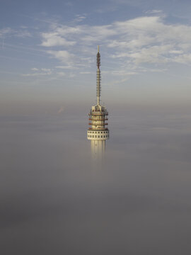 Aerial view of the Roermond TV Tower rising above a thick layer of morning fog under a clear blue sky in Roermond, Limburg, Netherlands.