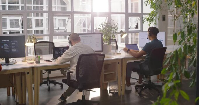 Coworkers typing fixing headset, reaching items at desk in office after alert holding phone smiling