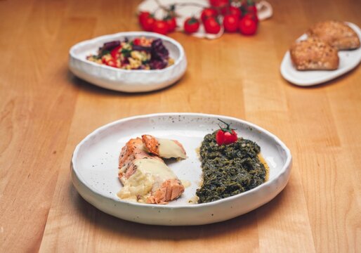 Plated food with spinach, chicken, tomatoes, and dessert on a wooden table highlighting food presentation during a meal associated with food crises awareness and solutions