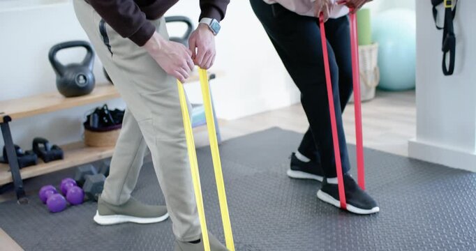 African American men at home gym using loop bands under feet, hinging for strength while coaching