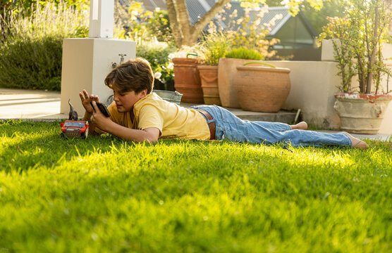 young teenage film maker using smart phone to make a dinosaur movie on his lawn at sunset