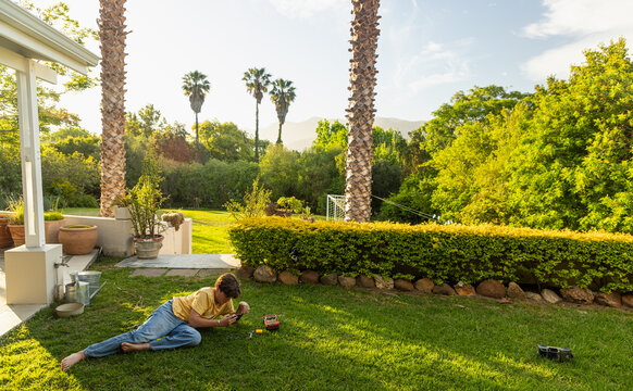 young teenage film maker using smart phone to make a dinosaur movie on his lawn at sunset