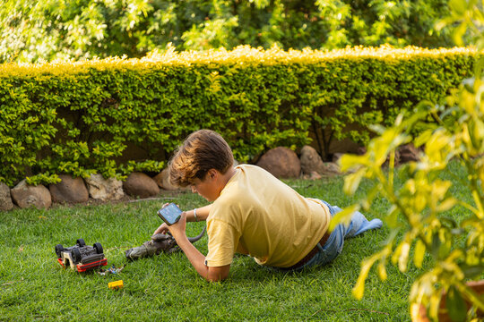 young teenage film maker using smart phone to make a dinosaur movie on his lawn at sunset