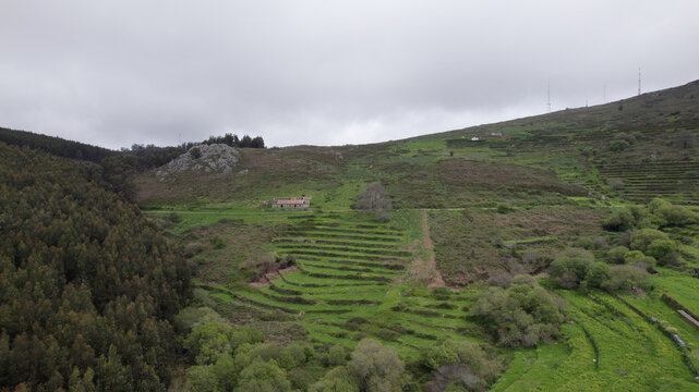 Aerial view of terraced fields and lush green hills in the Monchique mountain range, featuring a small stone building nestled in the landscape of Monchique, Faro, Portugal.