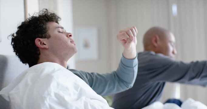 Male roommates waking to daylight through blinds, stretching on bed and checking smartphone