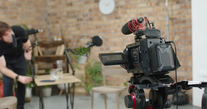 Male host leaning over table at loft, adjusting mic, camera and props while preparing for recording