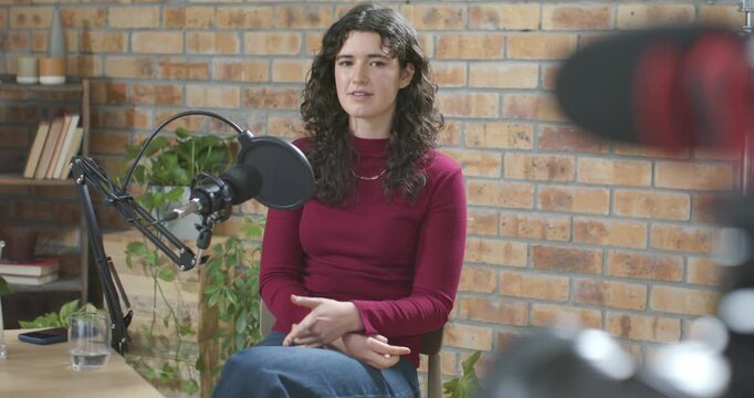 Woman in her 20s responding to off-frame prompt, speaking into condenser microphone at brick studio