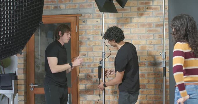 Diverse crew assembling tall C-stand and lamp while passing cables, preparing for shoot in studio