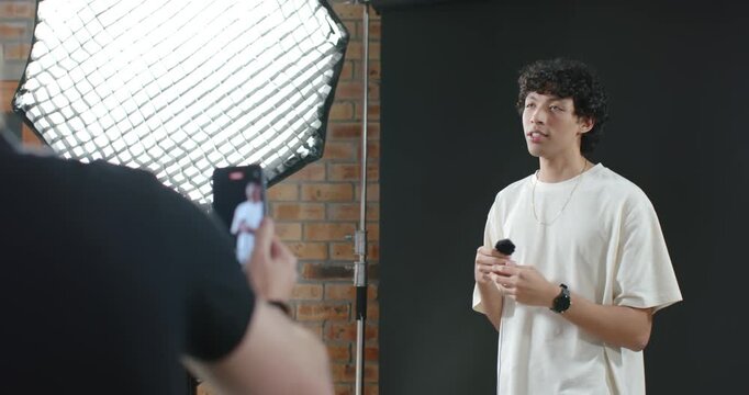 Diverse colleagues using softbox, cameraman framing smartphone, presenter holding mic for recording