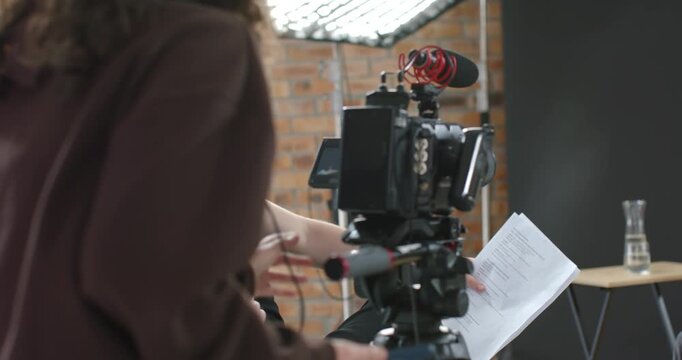 Film crew entering frame, adjusting camera rig while seated man pointing script, prepping take