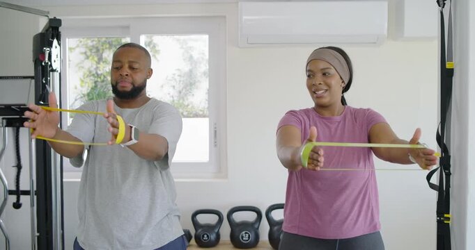 Couple starting holding yellow looped bands, pushing and pulling in sync in home gym for strength